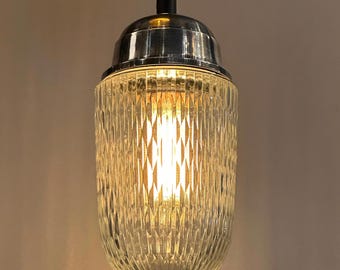May include: A silver pendant light with a clear, ribbed glass shade. The light is turned on and illuminates the room.