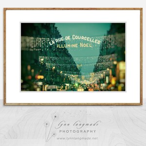 May include: A framed photograph of a street scene at night, with strings of lights illuminating the words "LA RUE DE COURCELLES ILLUMINE NOEL". The image has a vintage, soft focus effect, with buildings lining the street.