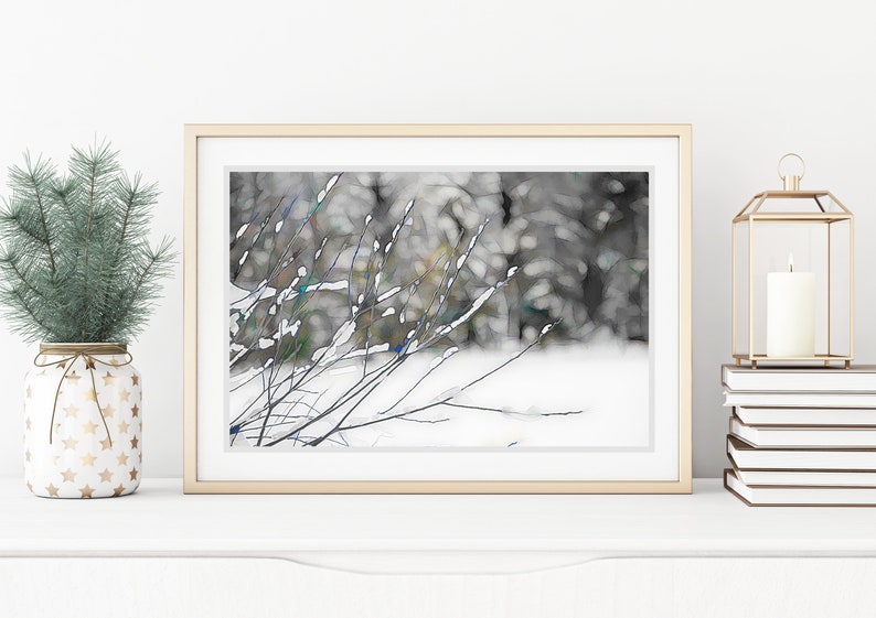 Op de afbeelding: Een ingelijste kunstdruk met een winterlandschap met besneeuwde takken. Het kunstwerk zit in een gouden lijst en wordt op een wit oppervlak weergegeven. Een kleine kerstboom in een decoratieve pot en een kaars in een gouden lantaarn staan ook op het oppervlak.