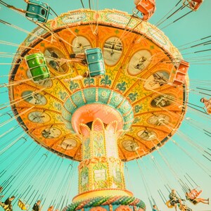 May include: A colorful amusement park swing ride against a bright blue sky. The ride features a large, ornate canopy with intricate designs in shades of yellow, orange, and green. Passengers are seated in individual swings.
