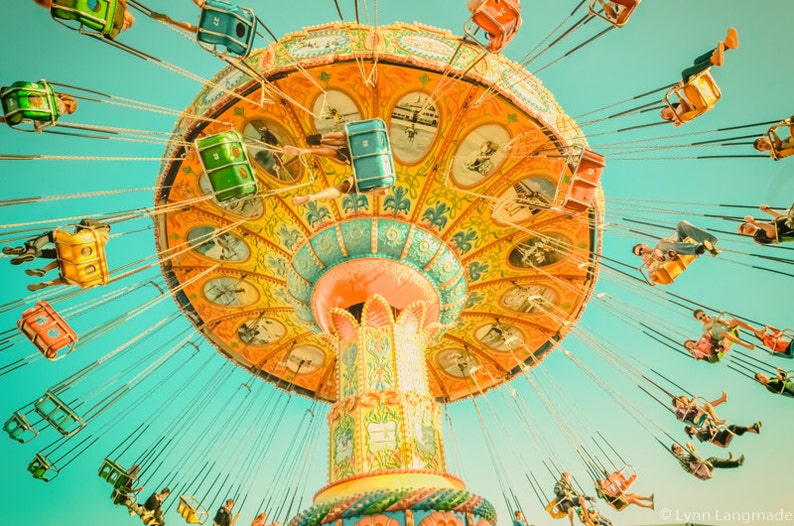 May include: A colorful amusement park swing ride against a bright blue sky. The ride features a large, ornate canopy with intricate designs in shades of yellow, orange, and green. Passengers are seated in individual swings.