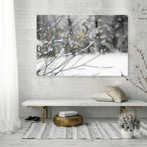 Op de afbeelding: Een winterlandschapsfoto met besneeuwde takken tegen een vage bosachtergrond. Het kunstwerk hangt boven een witte bank met gouden poten, een gestreept tapijt en decoratieve items. De afbeelding is gesigneerd "Lynn Langmade PHOTOGRAPHY".