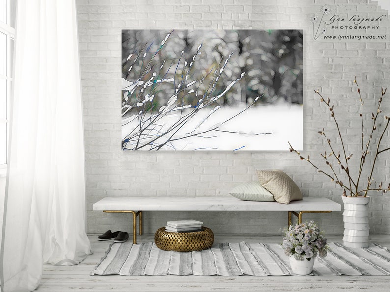 Op de afbeelding: Een winterlandschapsfoto met besneeuwde takken tegen een vage bosachtergrond. Het kunstwerk hangt boven een witte bank met gouden poten, een gestreept tapijt en decoratieve items. De afbeelding is gesigneerd "Lynn Langmade PHOTOGRAPHY".