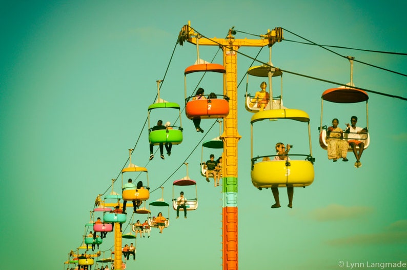 May include: A vintage-toned image of a colorful amusement park ride. Several gondolas in shades of green, orange, yellow, and pink are suspended from a tall, yellow support structure. People are riding in the gondolas against a teal sky.