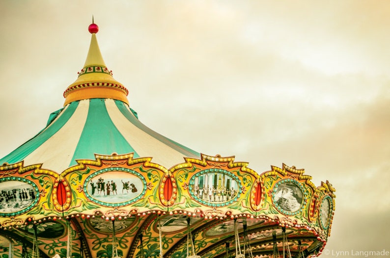 May include: A colorful carousel roof with a striped teal and white canopy. The ornate trim features painted scenes and is accented with gold and red details. A red ball tops the carousel's spire.