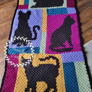 May include: A crocheted blanket with a colorful geometric pattern featuring black cat silhouettes. The blanket is made with a textured stitch and has a black border.