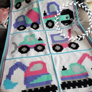 May include: A crocheted baby blanket with a white background and colorful squares featuring different construction vehicles. The squares are outlined in blue and the blanket has a colorful border.