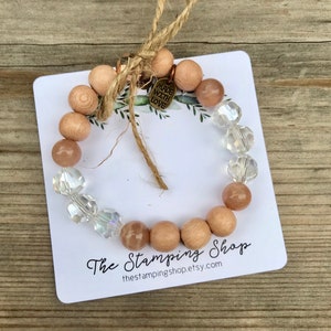 May include: A bracelet made with wood beads, sunstone beads, and crystal beads. The bracelet is tied with twine and has a small metal tag that says "Made with Love". The bracelet is displayed on a white card with the text "The Stamping Shop" and the website address "thestampingshop.etsy.com".