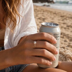 May include: A silver ring featuring a single small white pearl set in a delicate wire-wrapped band. The ring is worn on a finger, showcasing the metallic luster of the band and the smooth, round surface of the pearl against the silver setting.