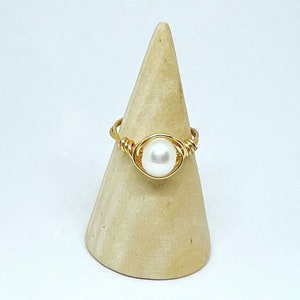 May include: A gold wire wrapped ring with a white pearl in the center.