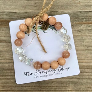 May include: A bracelet made with natural wood beads, clear crystal beads, and sunstone beads. The bracelet has a small charm that says "Made with Love". The bracelet is displayed on a white card with the text "The Stamping Shop" and the website address "thestampingshop.etsy.com".