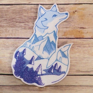 May include: A blue and purple embroidered patch of a fox with a mountain range inside its body. The fox is sitting with its tail curled around its body.