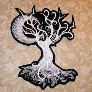 May include: Black and white embroidered patch of a stylized tree with a crescent moon in the branches. The tree is outlined in black and the branches and trunk are white.