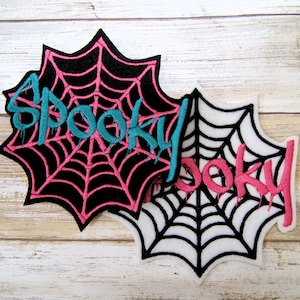 May include: Two black and white embroidered patches with a spiderweb design and the word "Spooky" in pink and teal lettering.