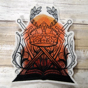 May include: Embroidered patch with a black and white design of a crown, two swords, and a book. The background is a gradient of orange and red.