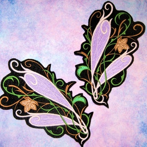 May include: Two embroidered iron-on patches featuring a pair of purple and white wings with black, green, and brown floral designs.
