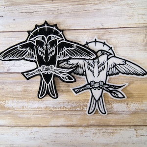 May include: Two embroidered iron-on patches featuring black and white stylized birds perched on branches. The black bird has two heads and a halo. The white bird has a single head and a halo.