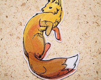 May include: A yellow and orange embroidered patch of a fox curled up with its tail wrapped around its body. The fox has a white tip on its tail.