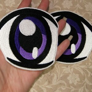 May include: Two white and black embroidered iron-on patches of anime eyes with purple irises.