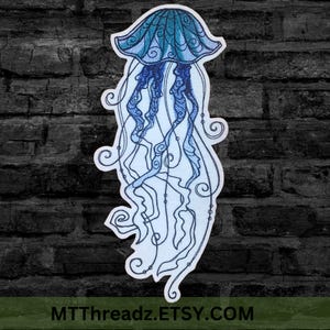 May include: An embroidered iron-on patch depicting a blue and teal jellyfish with intricate details. The jellyfish has a bell-shaped head and long, flowing tentacles.
