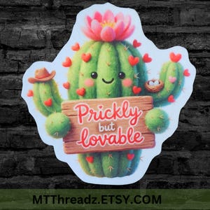May include: A sticker featuring a cartoon cactus with a smiling face, red heart accents, and a pink flower. The cactus holds a wooden sign that reads "Prickly but lovable". A small bird's nest with eggs is also visible.