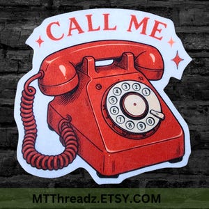May include: A die-cut sticker featuring a bright red vintage rotary telephone with a coiled cord. Above the telephone, the text CALL ME is printed in red capital letters, flanked by two small four-pointed star icons on a white background.