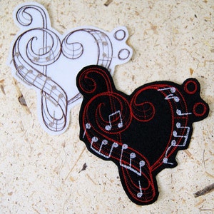 May include: Two embroidered patches in the shape of a heart with musical notes and a treble clef. One patch is white with brown embroidery and the other is black with red and white embroidery.