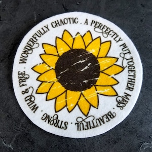 May include: A white round coaster with a sunflower design and the text "WONDERFULLY CHAOTIC. A PERFECTLY PUT TOGETHER MESS. BEAUTIFUL. STRONG. WILD & FREE" around the sunflower.