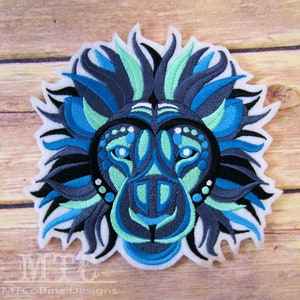 May include: A blue, green, and black embroidered lion head patch. The lion's mane is made of stylized, flowing lines. The lion's face is detailed with intricate patterns.