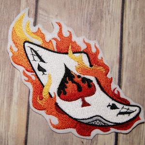 May include: Embroidered patch of an ace of spades playing card engulfed in flames. The card is white with black spades and a red ace. The flames are orange and yellow.