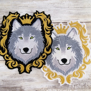 May include: Two embroidered patches featuring a wolf's head with a crown above it. The wolf's head is gray with black fur and green eyes. The patches are surrounded by a gold embroidered frame.