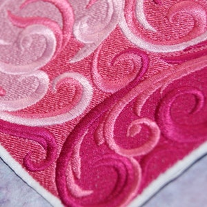 May include: A close-up of a pink and white embroidered fabric with a swirling pattern.