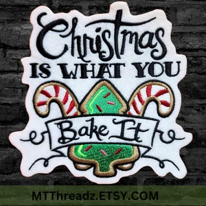 May include: White embroidered patch with the text "Christmas is what you bake it" in black cursive font. A green gingerbread tree with red and white candy canes is in the center of the patch.