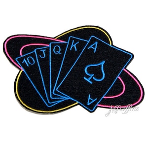 May include: An embroidered patch featuring a black felt background with a neon pink and yellow ring around the edge.  Five playing cards are arranged in a fan shape, with the 10, Jack, Queen, King, and Ace of Spades visible.  The cards are outlined in blue thread.