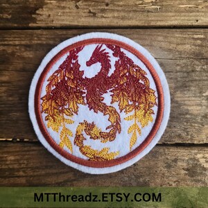 May include: Embroidered patch featuring a stylized phoenix in shades of red and gold, encircled by a brown border. The phoenix is surrounded by leaf-like details, all set against a white background. The patch has a white border and the text MTThreadz.ETSY.COM.