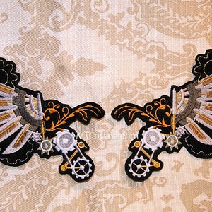 May include: Two black embroidered patches with silver and gold gears and wings. The wings are made of multiple layers of fabric and have a steampunk aesthetic.