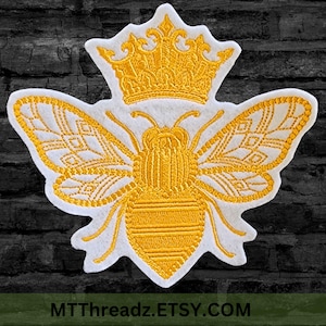 May include: Embroidered patch featuring a golden bee wearing a crown. The bee has detailed wings and body, set against a white background. The patch is likely for clothing or accessories. The text "MTThreadz.ETSY.COM" is at the bottom.