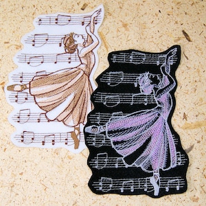 May include: Two embroidered iron-on patches featuring a ballerina dancing on a musical staff. One patch is on a white background with brown embroidery, and the other is on a black background with silver embroidery.