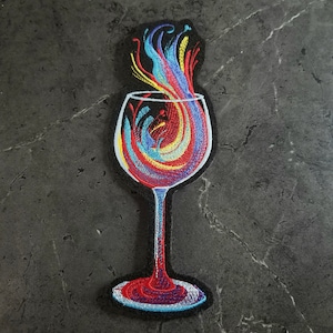 May include: A colorful embroidered patch of a wine glass with a swirling design of red, yellow, blue, and purple.