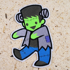 May include: Green Frankenstein monster cartoon character with black hair, gray jacket, blue jeans, and stitched details. The monster is smiling and has a green face with stitched scars.