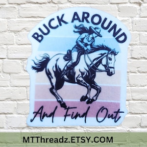 May include: A sticker with a vintage-style design featuring a woman riding a horse. The text on the sticker reads "Buck Around And Find Out" and "MTTThreadz.ETSY.COM".