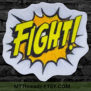 May include: A white sticker featuring a comic book style design with the word "FIGHT!" in bold yellow letters with a black outline. The word is set against a yellow burst, with a jagged edge. The sticker is die-cut.