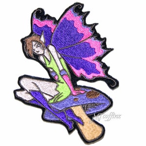 May include: Embroidered iron-on patch featuring a fairy with purple wings sitting on a mushroom. The fairy is wearing a green dress and purple boots. The mushroom is brown and purple.