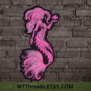 May include: Pink embroidered mermaid patch with intricate details. The mermaid has long flowing hair and a tail with a swirling design. The patch is on a black background.