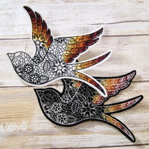 May include: Two embroidered bird appliques in a black and white lace design. The top bird has orange and red wings, while the bottom bird has black and orange wings.