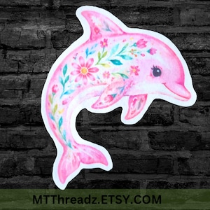 Peut inclure: Un autocollant dauphin rose orné d'un motif floral composé de diverses fleurs et de feuilles vertes sur tout le corps. Le dauphin est représenté en position de saut avec une bordure blanche. Le texte MTTTHREADZ.ETSY.COM est inscrit en bas.