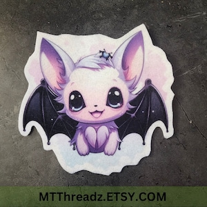 May include: A cute cartoon bat with purple fur, big eyes, and black wings. The bat is sitting on a cloud with a small spider on its head.
