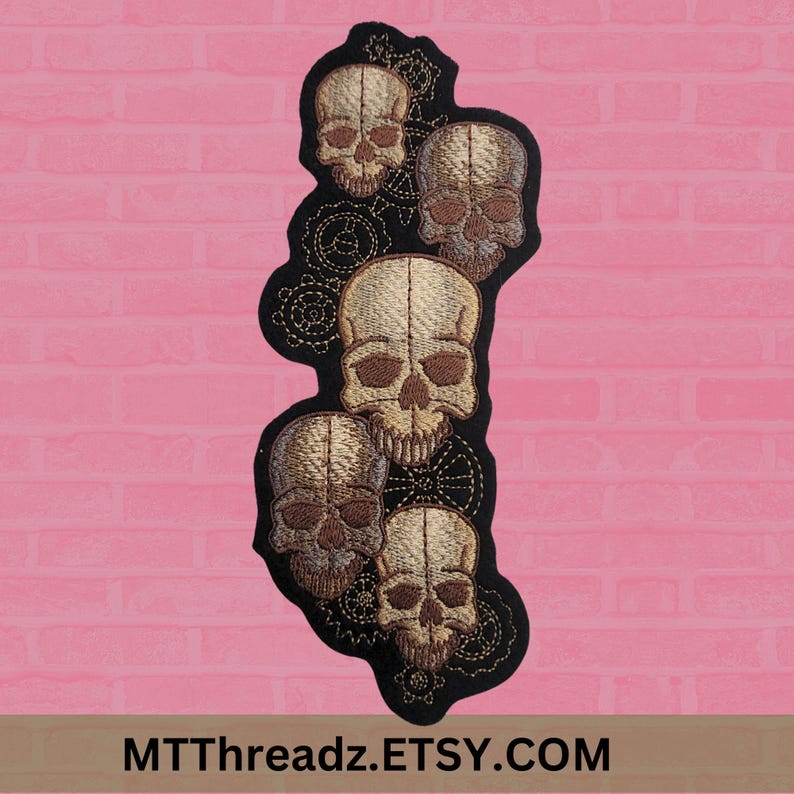 K&ouml;nnte beinhalten: Gestickter Aufn&auml;her mit f&uuml;nf braunen Sch&auml;deln und filigranen Zahnrad-Designs auf schwarzem Hintergrund.
