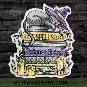 May include: Embroidered patch of a gray cat wearing a purple witch hat, sleeping on top of a stack of books. The books have the words "Spells", "Potions", and "Elixirs" on their spines. The patch is surrounded by green leaves and yellow candles.