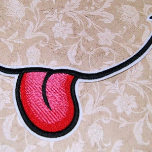 May include: Embroidered iron-on patch of a cartoon mouth with a red tongue sticking out. The mouth is outlined in black and white.